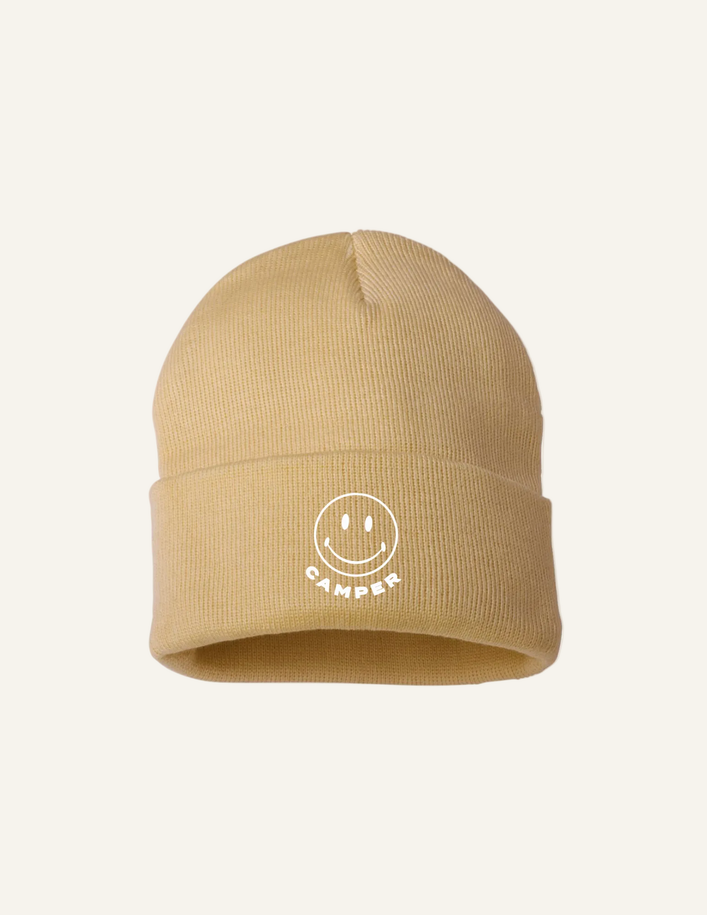 A beige beanie hat with a smiley face and the text 'CAMPER' written underneath it.