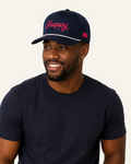 A man wearing a navy blue crewneck t-shirt and a matching navy blue baseball cap with 'Happy' embroidered in red script on the front, photographed against a light gray studio background.