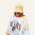 Person wearing a 'Chicago Bears' sweatshirt and a beige cap with 'HAPPY' text on a white background