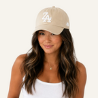 A woman wearing a beige baseball cap with a white embroidered 'ZA' logo on the front and a small white side logo, paired with a white ribbed tank top against a plain white background.