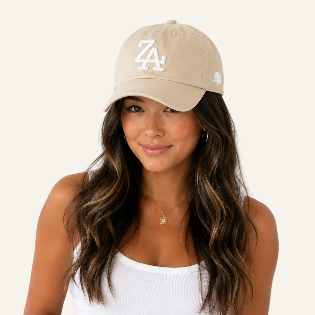 A woman wearing a beige baseball cap with a white embroidered 'ZA' logo on the front and a small white side logo, paired with a white ribbed tank top against a plain white background.